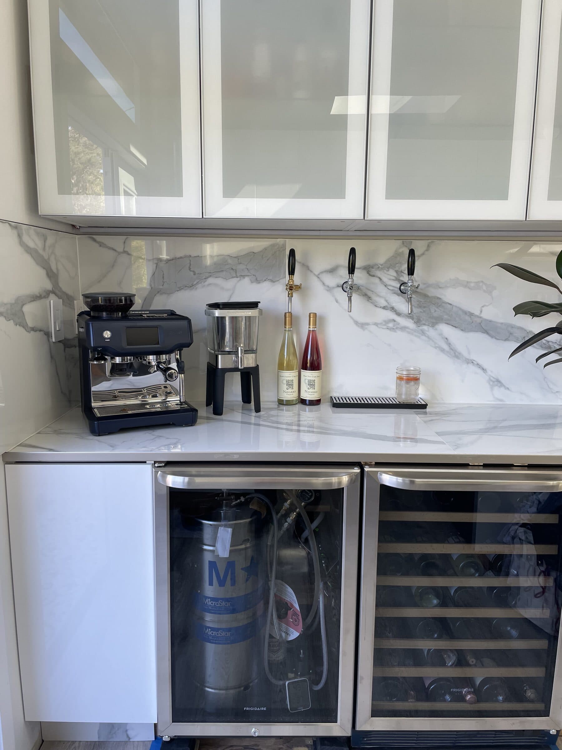 The built-in bar — two wine fridges, wall-mounted beer spigots, a carbonator, and an espresso machine against marble tile