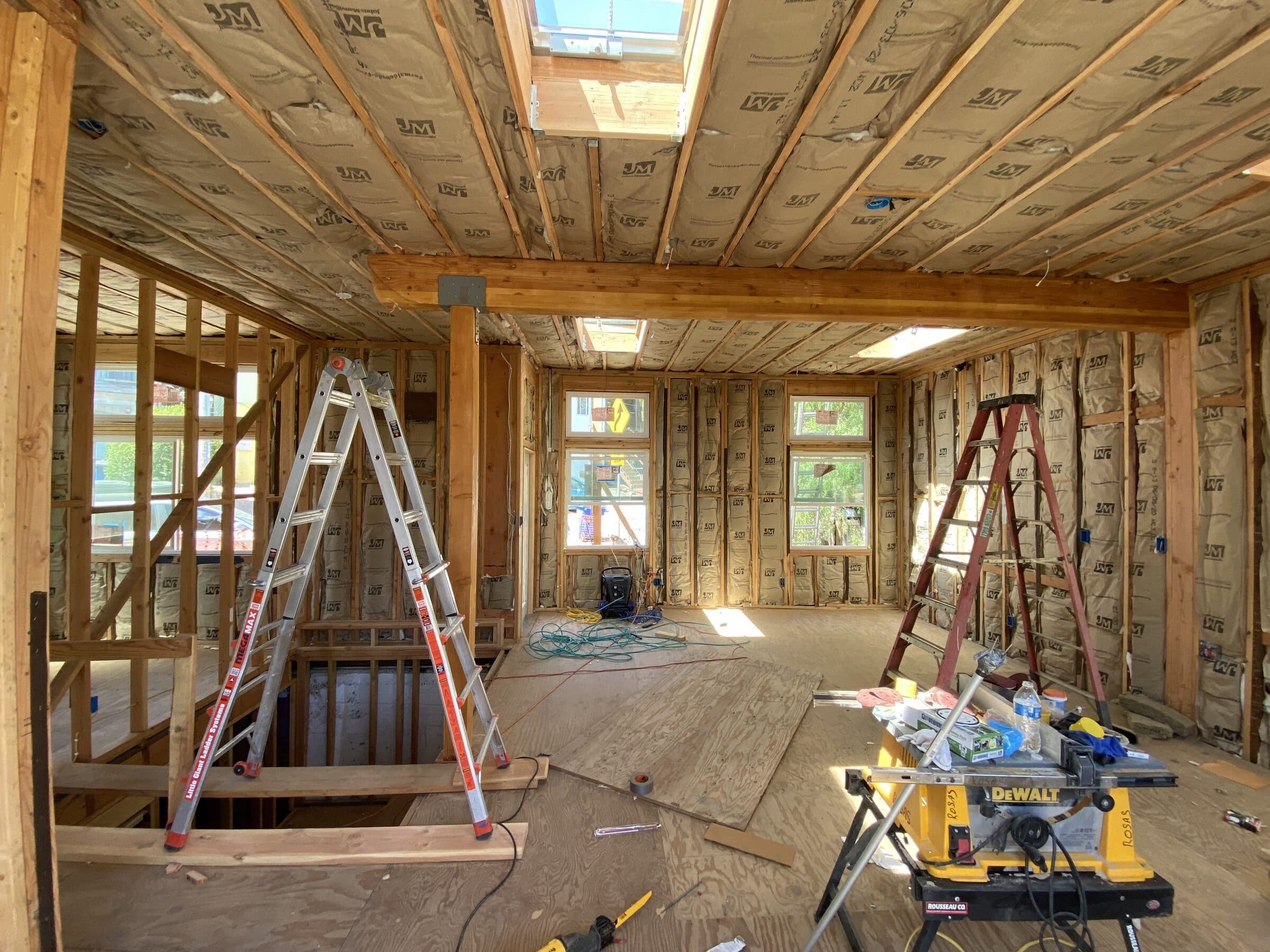 Interior during construction — insulated stud walls, exposed glulam beam, skylights, and rough openings