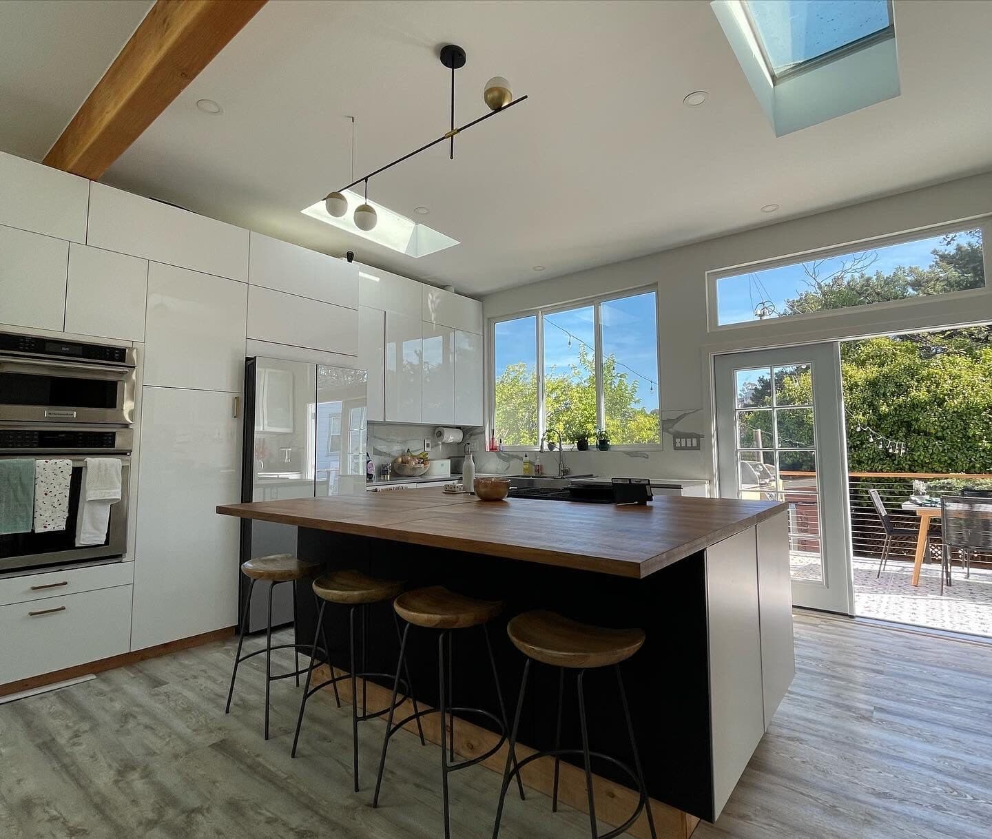The finished upstairs: an open kitchen under an 11-foot ceiling with a glulam beam, skylights, and a wall of glass to the deck