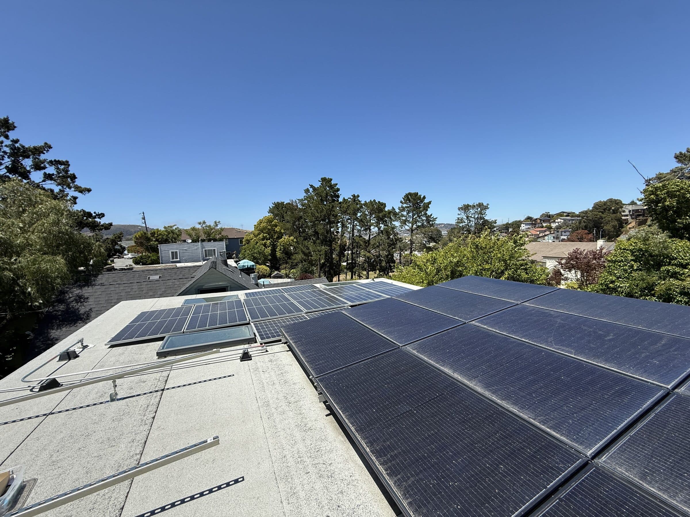 Solar panels across the skillion roof — two arrays flanking the operable skylights, with the Bay Area hills beyond